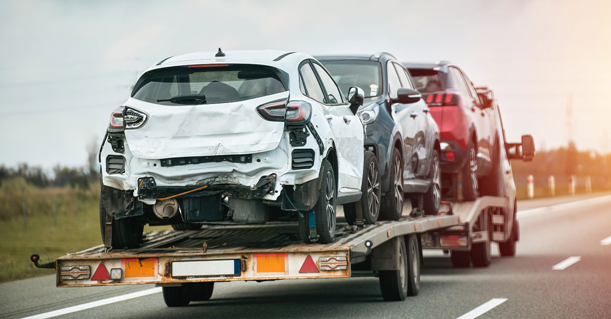 Three wrecked cars being towed away on a tow truck.