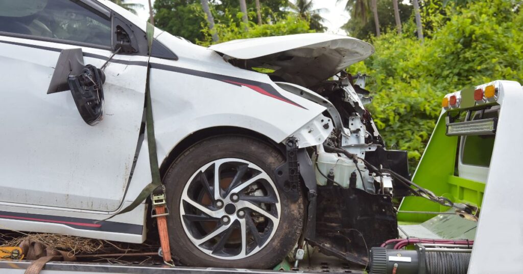 Damaged white car secured on a tow truck for vehicle removal and wrecking.